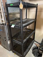 Black four-shelf plastic utility shelving unit in basement setting