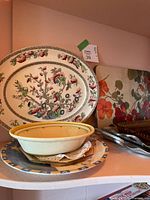 Shelf view showing oval fruit platter, yellow-rim bowl, stack of plates