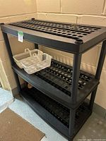Front view of 3-tier black plastic shelf with basket on middle tier