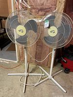 Two Hampton Bay pedestal fans standing side by side