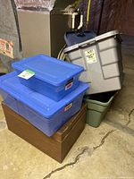 Stack of plastic totes (gray, green, two blue) and wooden chest at bottom