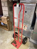 Full view of red steel hand truck showing frame, handle, wheels, and toe plate
