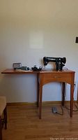 Full view of sewing machine mounted in wood cabinet with attachments tin and accessories on top