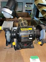 Full view of Worksmith bench grinder showing dual wheels, eye shield, work light, and base controls