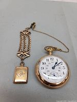 Pocket watch, chain and locket arranged flat showing dial and full assembly