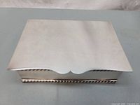 Closed rectangular silver-plated box showing scalloped front lid and rope trim