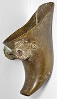 Side view of brass shoe-shaped planter showing patina and iron lace ornament