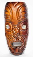 Front view of hand-carved wooden Maori mask with paua shell eyes