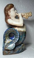 Right side view of mermaid sculpture showing curled tail and conch horn