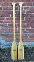 Full view of both wooden paddles leaning against brick wall