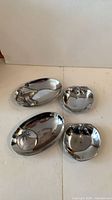 Four polished aluminum Mariposa serving dishes (two oval platters, two round bowls) top view