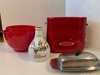 Lot overview showing hot dog maker, three red bowls, olive oil cruet, stainless butter dish