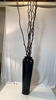 Full view of black metal vase with tall curly twigs