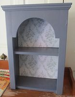 Front view showing arched opening, shelves and wallpaper back