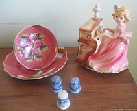 Group shot of music box figurine, teacup, saucer, three thimbles