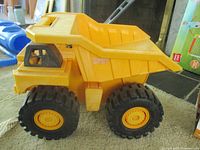 Left side view of yellow plastic dump truck toy showing dump bed and wheels