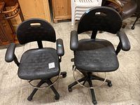Both black polyurethane drafting chairs showing overall design with foot rings and casters