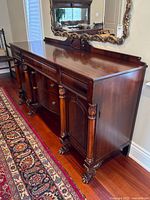 Full view of flame mahogany sideboard showing bow-front drawers, cabinet doors, carved clawfoot legs and backsplash mirror