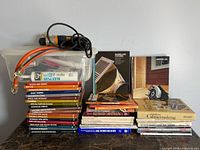 Overall view of books stacked, drill on plastic bin, additional books at right