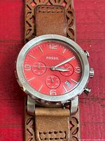 Watch face showing red dial, subdials, bezel and part of strap