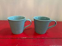 Front view of both light blue mugs side by side showing exterior color and ribbed texture