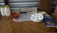 Entire lot on table showing bacon crispers, egg poacher, plates, pastry mat, plastic bottles, cookbooks