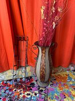 Tall metal vase with faux florals and part of iron planters visible