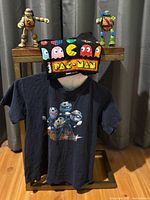 Full lot: two TMNT figures, Pac-Man tee on table, TMNT tee hanging