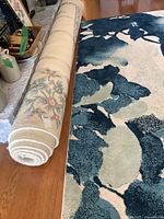 Rolled rug beside another rug, showing ivory color and floral design tag
