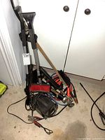 Group of snow brushes, booster cables, charger, grease gun and inflator on floor