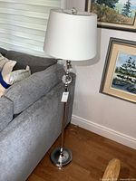 Full view of chrome floor lamp beside sofa with white drum shade