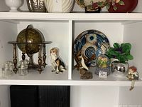 Overall view of shelf showing globe, dog figurine, plate, sculptures, faux flowers and more