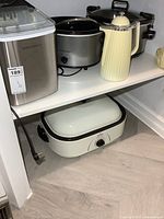 Group shot showing ice maker, two slow cookers, insulated coffee carafe on upper shelf and roaster oven on lower shelf