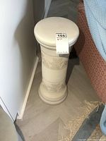 Full view of cream ceramic pedestal with floral relief, showing top and midsection detail