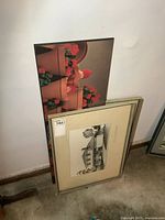 Two framed prints and one plaque board leaning against wall