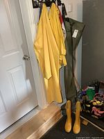 Full view of yellow raincoat, green chest waders, and yellow boots hanging by door