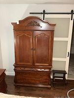 Front view of armoire dresser showing doors, drawers, carved crest