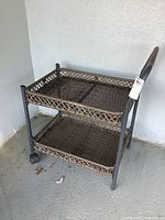 Front view of brown plastic wicker two-tier cart showing shelves, frame, and wheels