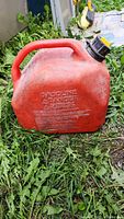 Red 10 L gas can lying on grass, showing embossed text