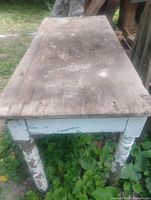 Angled view of table top and legs showing distressed paint and weathered surface
