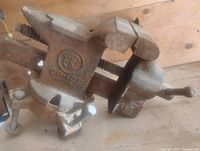 Side view of cast iron bench vise showing jaws, swivel base, screw handle, and logo