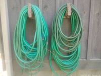 Two coiled green garden hoses hanging, showing overall condition and length