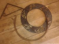 Overall view of ornate cast-iron collar and two iron brackets on wooden floor