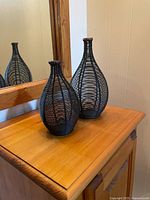 Two black metal wire vases on wooden surface, mirror background