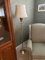 Full view of brass floor lamp beside armchair and cabinet