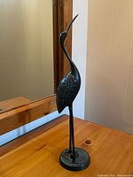 Full view of metal egret sculpture on table, showing overall form and base