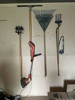 Group view of garden tools on pegboard including string trimmer, cultivator, squeegee, rakes and bow saw