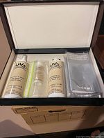 Open box showing contents: two UV3 bottles, sealed pouch, booklet inside brown box