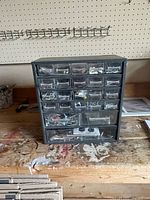 Front view of black plastic drawer cabinet showing multiple clear drawers filled with hardware