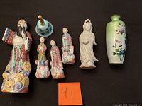Group of seven porcelain figurines and vase displayed on black surface